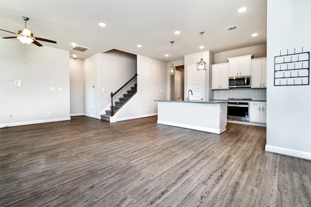 kitchen featuring appliances with stainless steel finishes, hanging light fixtures, an island with sink, white cabinets, and dark hardwood / wood-style flooring