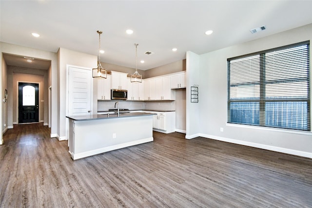 kitchen featuring an island with sink, wood-type flooring, white cabinets, decorative backsplash, and hanging light fixtures