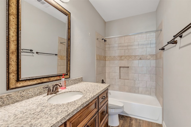 full bathroom with tiled shower / bath, vanity, wood-type flooring, and toilet