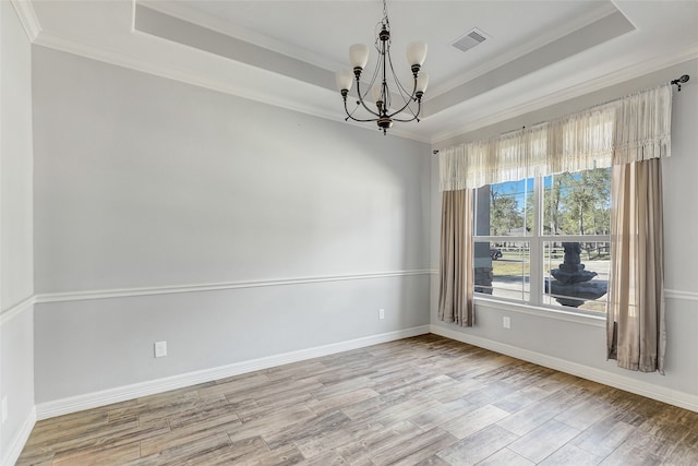 spare room featuring a notable chandelier, ornamental molding, a tray ceiling, and light hardwood / wood-style flooring