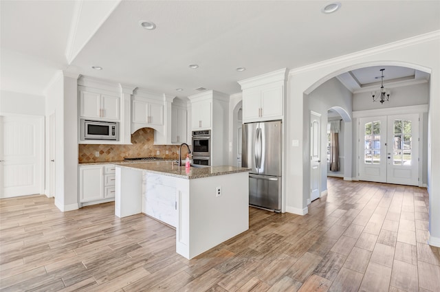 kitchen featuring white cabinets, appliances with stainless steel finishes, stone countertops, and a kitchen island with sink