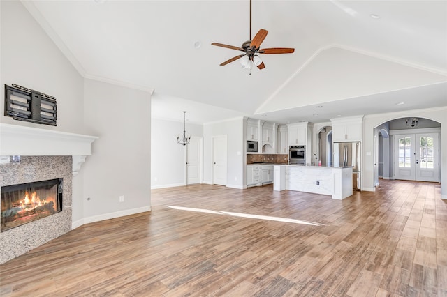 unfurnished living room featuring high vaulted ceiling, french doors, ceiling fan with notable chandelier, light wood-type flooring, and ornamental molding