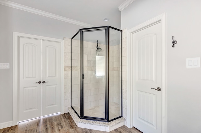 bathroom with wood-type flooring, a shower with shower door, and ornamental molding