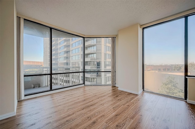 unfurnished room with a wall of windows, a textured ceiling, and light wood-type flooring