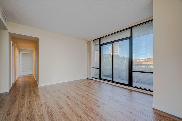 spare room with a textured ceiling, light hardwood / wood-style flooring, and floor to ceiling windows