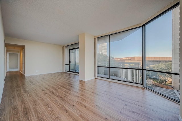 spare room with light hardwood / wood-style floors, a wall of windows, and a textured ceiling