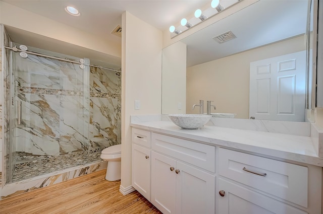 bathroom with a tile shower, vanity, wood-type flooring, and toilet