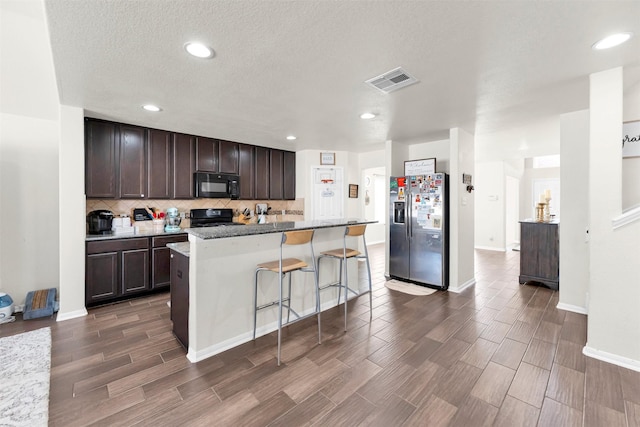 kitchen with dark brown cabinets, a center island, a breakfast bar, stone counters, and black appliances