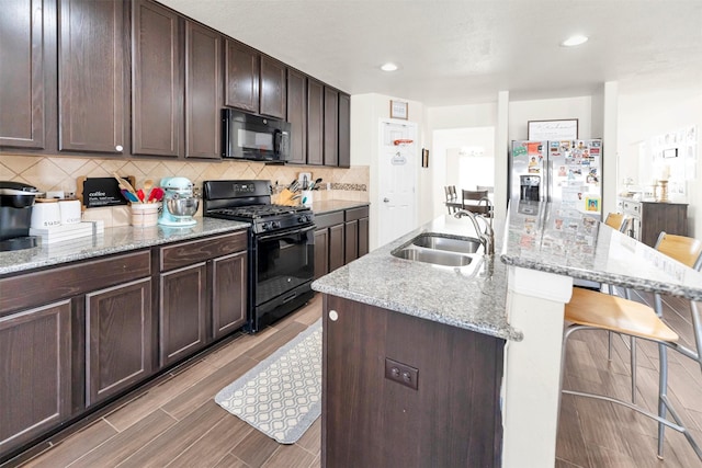 kitchen featuring dark brown cabinetry, black appliances, sink, a center island with sink, and a breakfast bar area