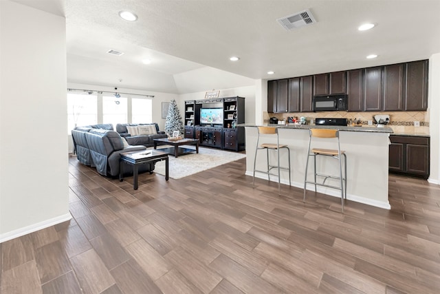 kitchen featuring a kitchen bar, wood-type flooring, dark brown cabinetry, and a kitchen island with sink