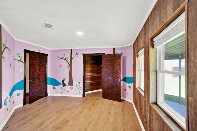 spare room featuring light hardwood / wood-style floors, crown molding, and wood walls