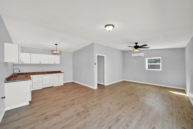 unfurnished living room with a wall mounted air conditioner, light wood-type flooring, ceiling fan, and sink