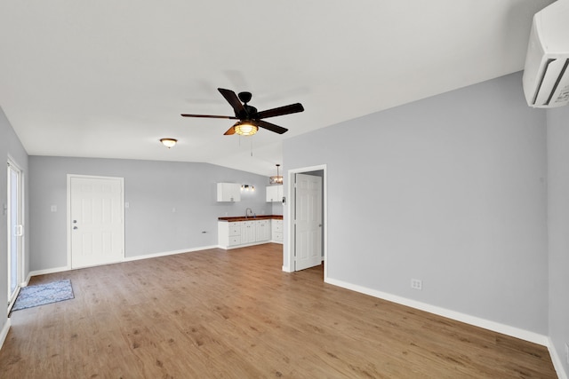 unfurnished living room with ceiling fan, sink, a wall mounted air conditioner, light hardwood / wood-style floors, and lofted ceiling