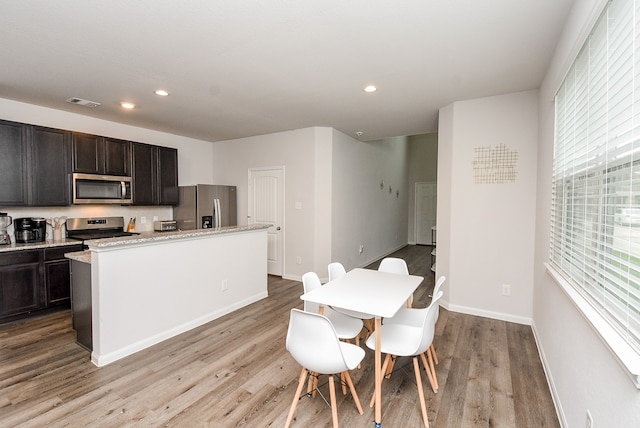 kitchen featuring light stone countertops, a center island, stainless steel appliances, dark brown cabinets, and light wood-type flooring