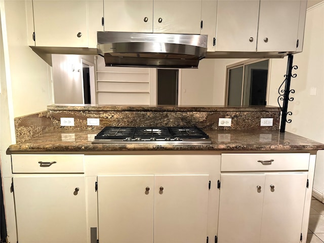 kitchen with stainless steel gas stovetop, white cabinets, dark stone countertops, light tile patterned floors, and extractor fan