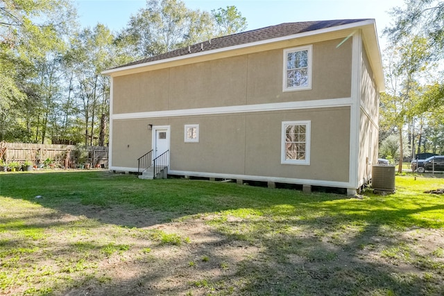 rear view of property featuring central AC unit and a lawn