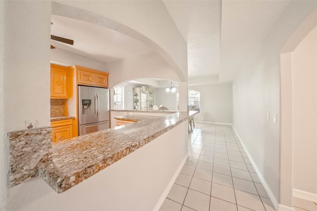 kitchen featuring light brown cabinets, stainless steel refrigerator with ice dispenser, kitchen peninsula, a textured ceiling, and light tile patterned flooring