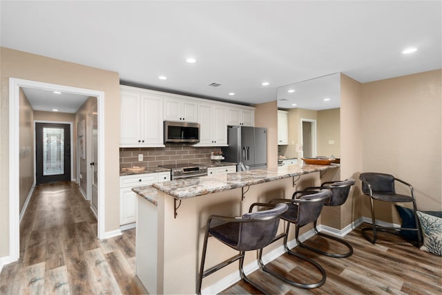 kitchen with light stone countertops, appliances with stainless steel finishes, a breakfast bar area, white cabinets, and light wood-type flooring