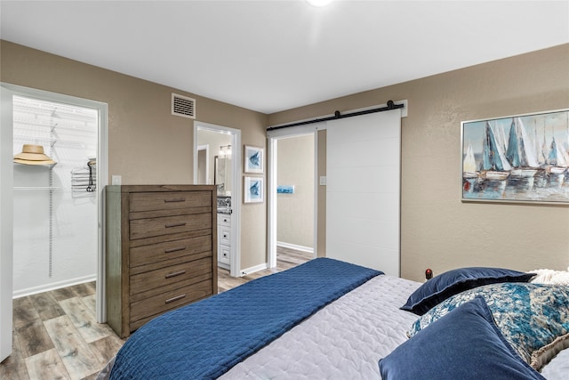 bedroom with a barn door, light hardwood / wood-style floors, and connected bathroom