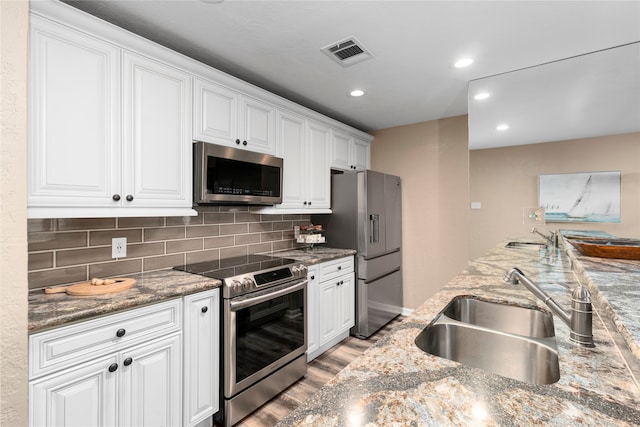 kitchen featuring white cabinetry, sink, light hardwood / wood-style floors, stone countertops, and appliances with stainless steel finishes