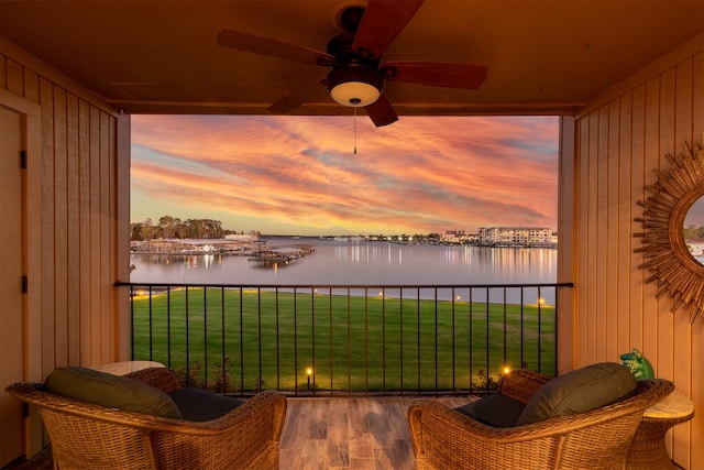 balcony at dusk featuring ceiling fan and a water view