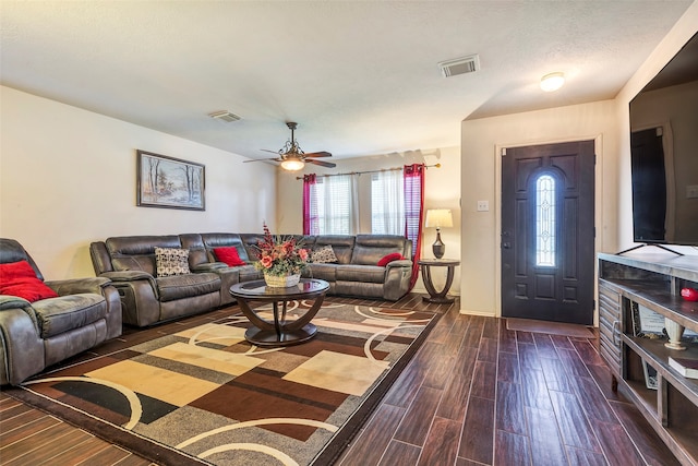 living room with a textured ceiling, ceiling fan, and dark wood-type flooring