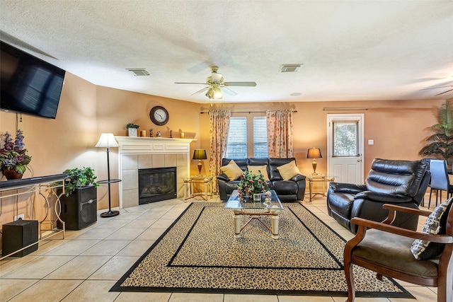 tiled living room with a tiled fireplace, ceiling fan, and a textured ceiling