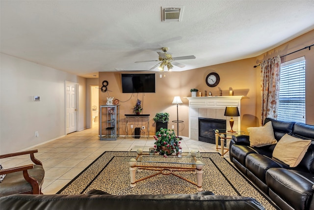 tiled living room featuring a fireplace, a textured ceiling, and ceiling fan