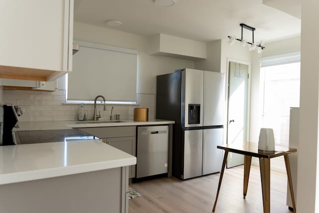 kitchen featuring white cabinetry, sink, light hardwood / wood-style flooring, pendant lighting, and appliances with stainless steel finishes