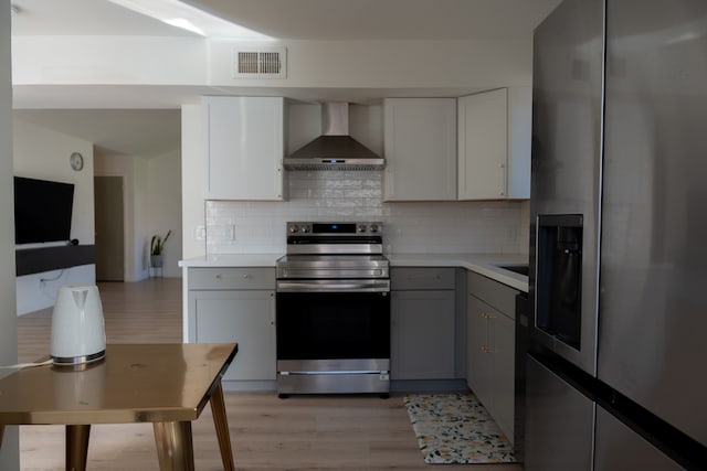 kitchen featuring tasteful backsplash, gray cabinetry, stainless steel appliances, wall chimney range hood, and light hardwood / wood-style flooring