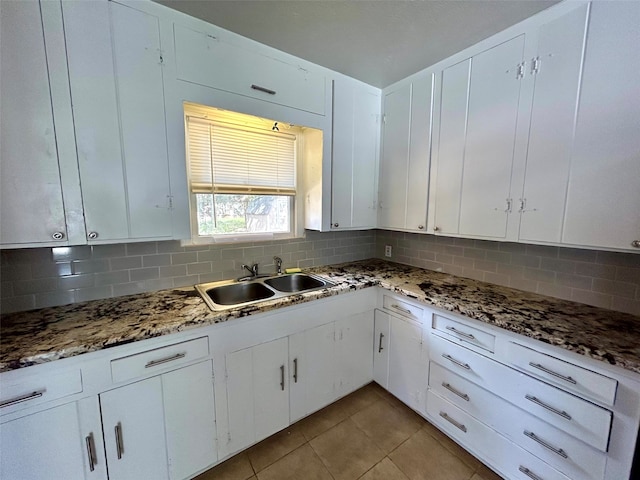 kitchen with sink, decorative backsplash, dark stone countertops, light tile patterned floors, and white cabinetry