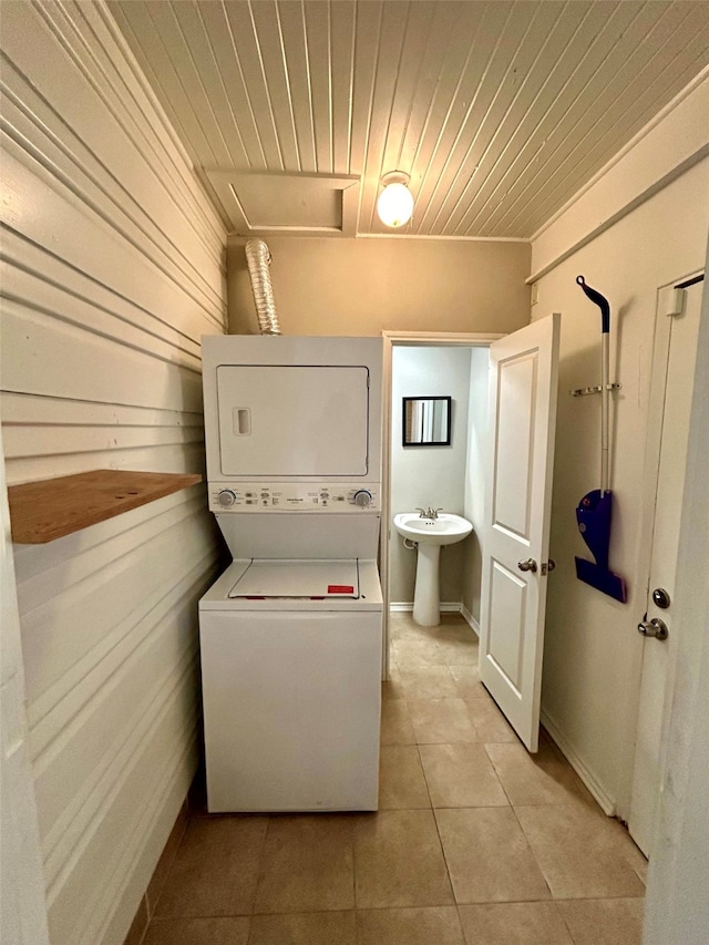 laundry area featuring light tile patterned floors, sink, stacked washer / drying machine, and wood walls