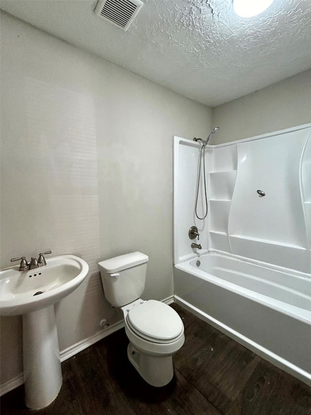 full bathroom with hardwood / wood-style floors, toilet, shower / washtub combination, and a textured ceiling