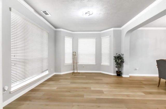 unfurnished room with crown molding, light wood-type flooring, and a textured ceiling