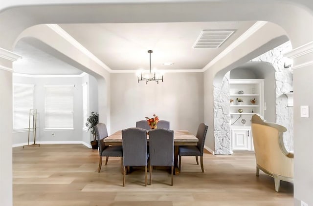 dining space with ornamental molding, light hardwood / wood-style flooring, a notable chandelier, and a stone fireplace