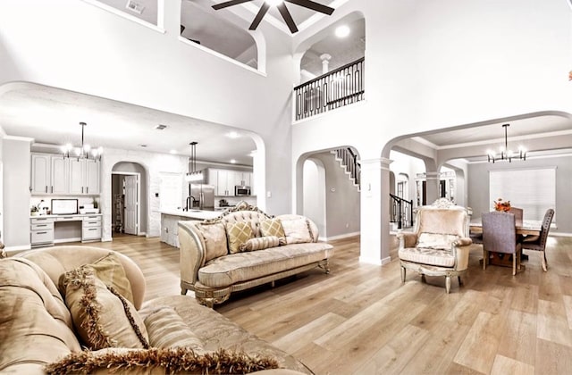 living room featuring a high ceiling, ceiling fan with notable chandelier, light hardwood / wood-style floors, and crown molding