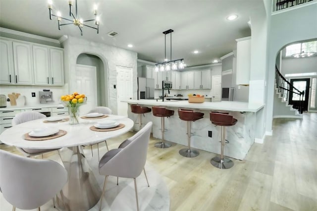 kitchen with white fridge with ice dispenser, a kitchen breakfast bar, light hardwood / wood-style flooring, pendant lighting, and white cabinets