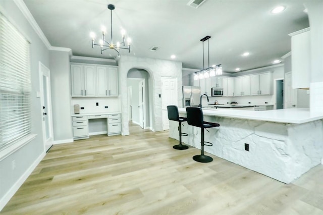 kitchen with appliances with stainless steel finishes, ornamental molding, light hardwood / wood-style floors, white cabinetry, and hanging light fixtures