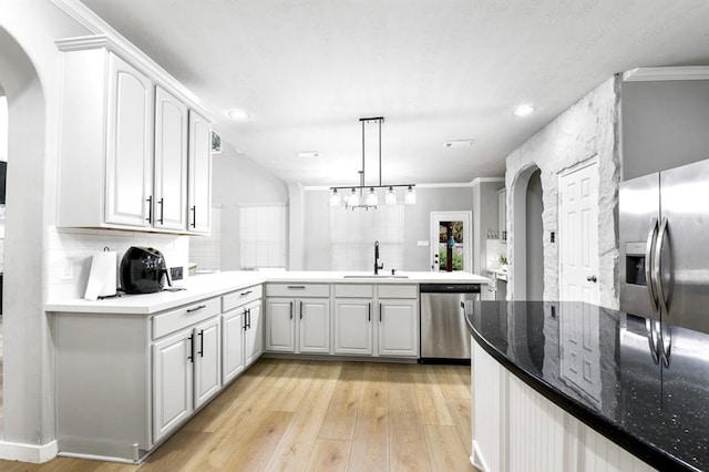 kitchen with white cabinets, kitchen peninsula, appliances with stainless steel finishes, and light hardwood / wood-style flooring