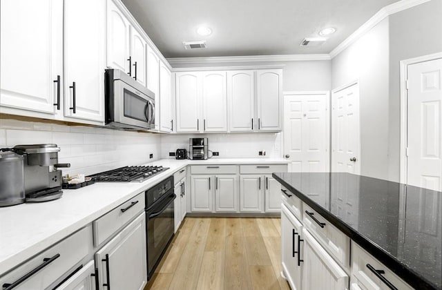 kitchen with light hardwood / wood-style flooring, crown molding, dark stone counters, white cabinets, and appliances with stainless steel finishes