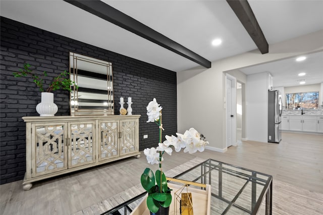 living room with beamed ceiling, sink, light hardwood / wood-style floors, and brick wall