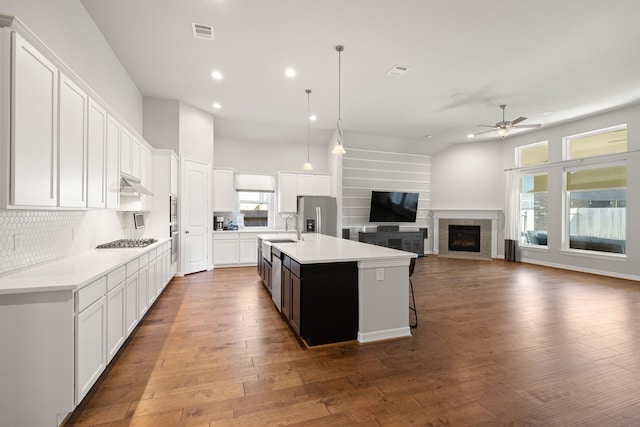 kitchen with stainless steel appliances, a kitchen island with sink, wood-type flooring, decorative light fixtures, and white cabinetry