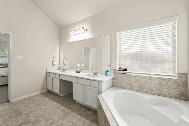 bathroom with tiled bath, a wealth of natural light, vanity, and lofted ceiling