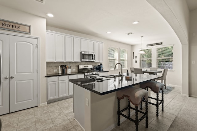 kitchen with stainless steel appliances, a kitchen island with sink, pendant lighting, white cabinets, and a breakfast bar area