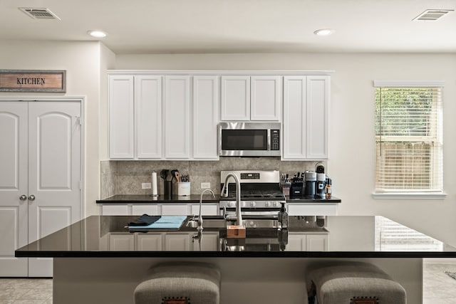 kitchen featuring a kitchen breakfast bar, white cabinets, an island with sink, and appliances with stainless steel finishes