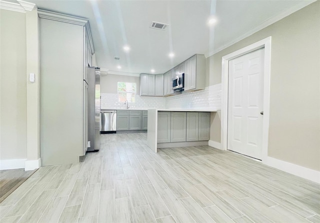 2222 Peppermill Rd, Houston, TX 77080 - kitchen with stainless steel appliances, gray cabinetry, light wood-style flooring, ornamental molding, and decorative backsplash