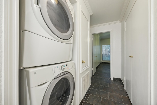 laundry area featuring stacked washer / dryer, dark tile patterned flooring, and ornamental molding