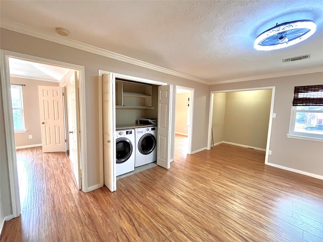 laundry room with a textured ceiling, washer and dryer, light wood-type flooring, and crown molding