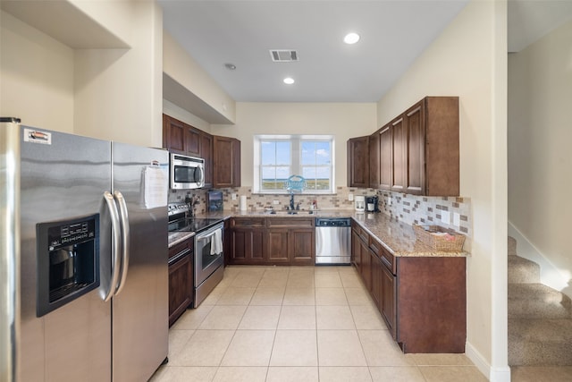 kitchen featuring light stone countertops, backsplash, stainless steel appliances, sink, and light tile patterned floors