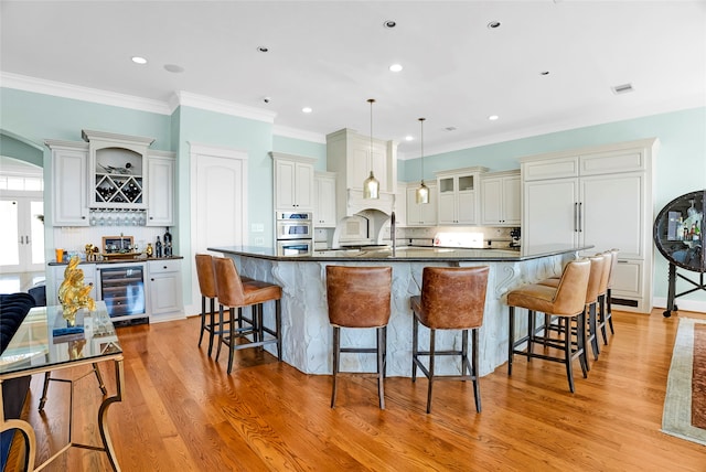 kitchen with hanging light fixtures, beverage cooler, a large island with sink, light hardwood / wood-style floors, and white cabinets